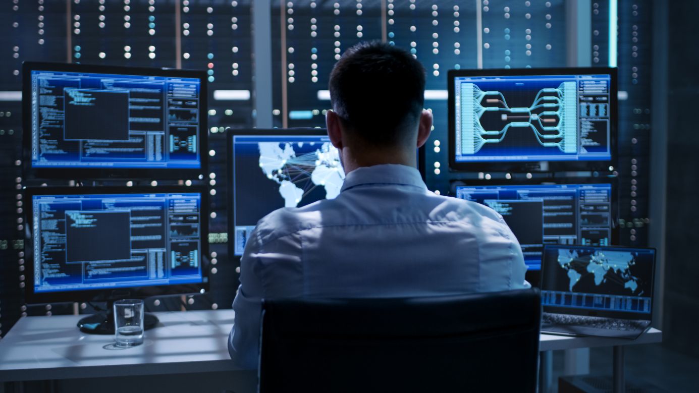 A man looking at multiple monitors, performing cybersecurity monitoring.