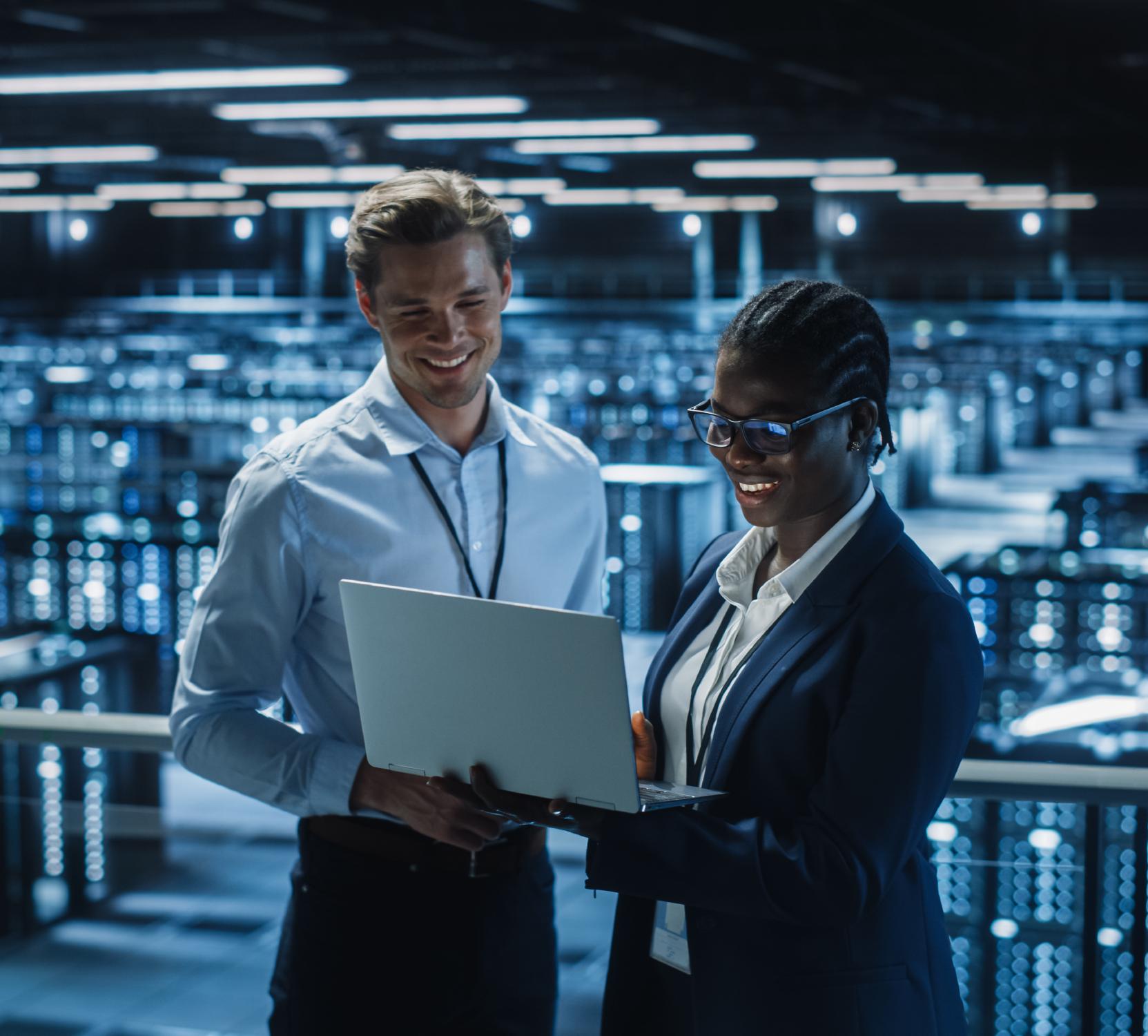 Two people working on a laptop in a server room.