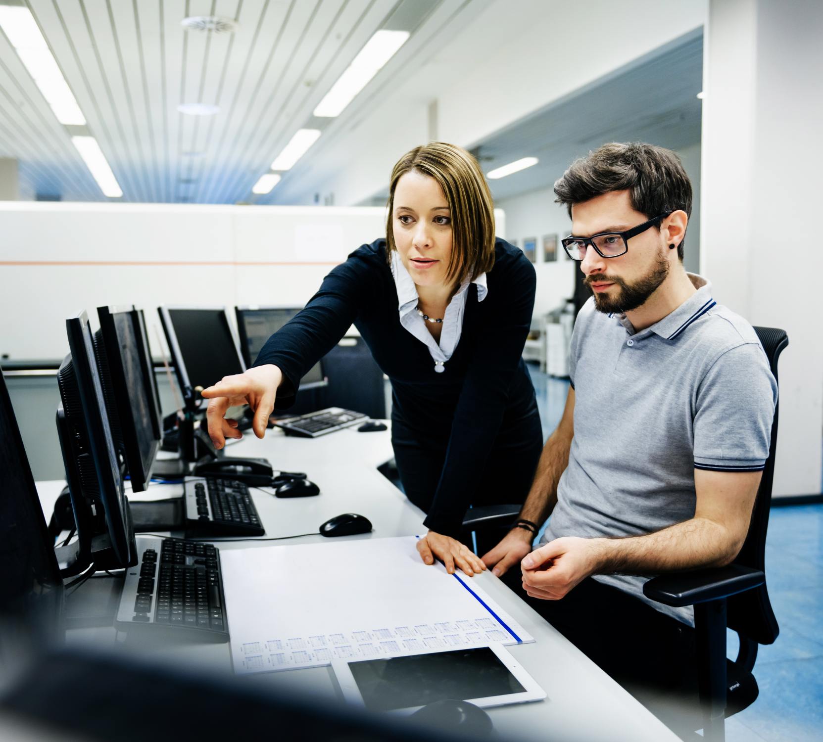 A man and woman looking at computer monitors.