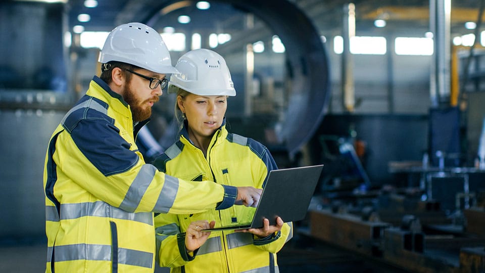 Male and Female Industrial Engineers in Hard Hats Discuss New Project while Using Laptop.